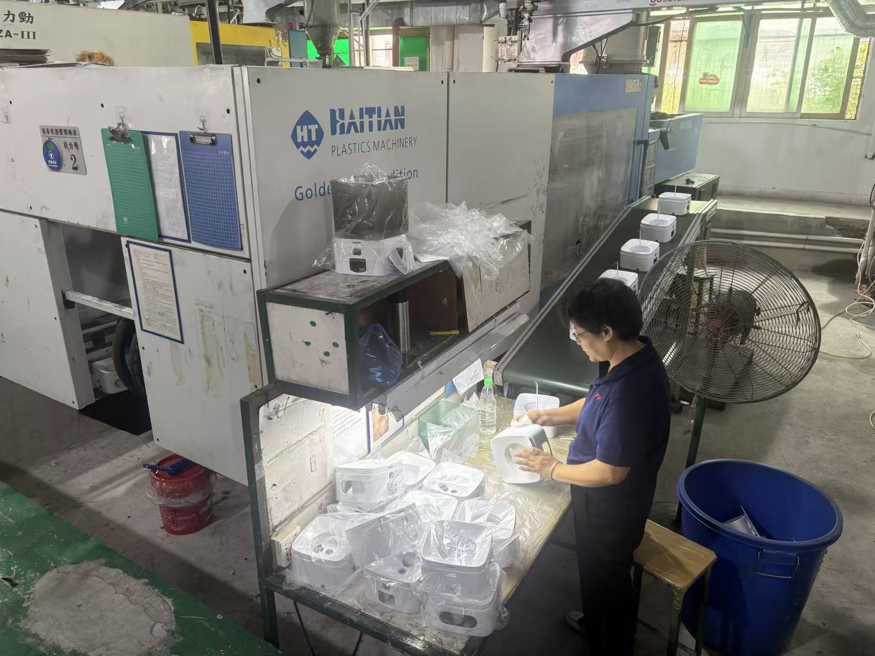 Worker handling molded white housings beside injection molding equipment